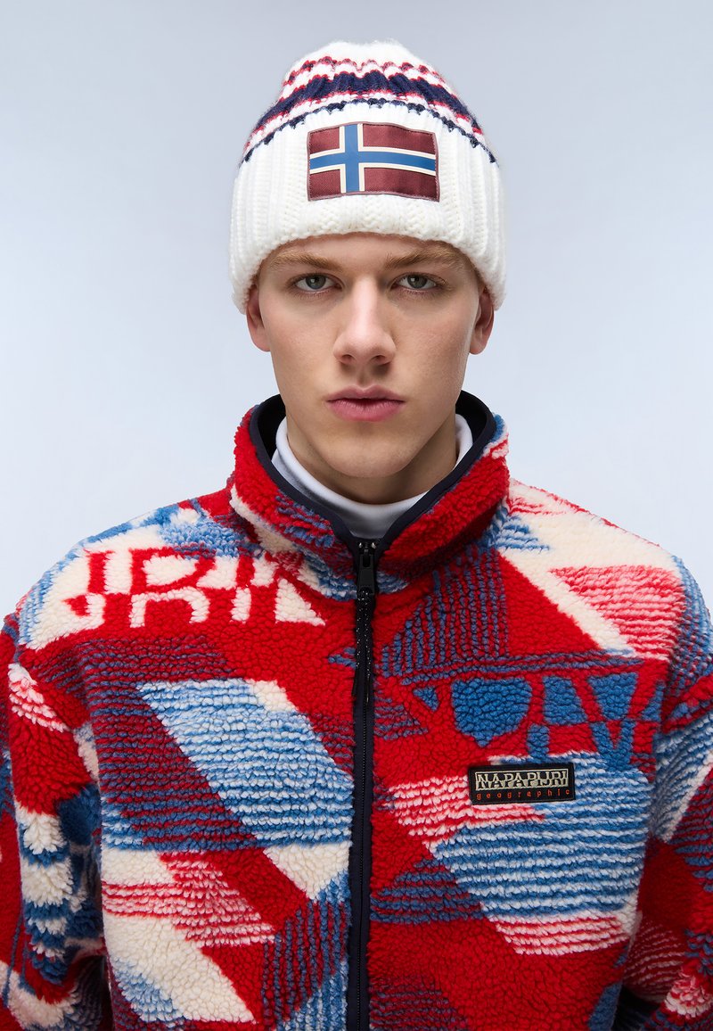 Giacca in pile a motivi rossi e blu con colletto alto e chiusura con zip; cappello lavorato a maglia bianco con patch della bandiera norvegese e accenti blu.