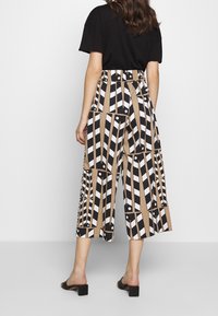 Wide-leg, high-waisted culottes featuring a geometric black and white pattern on a tan background. Smooth fabric, ankle-length design.