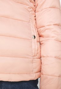 Giacca puffer rosa chiaro con design a righe orizzontali, dettagli con bottoni a pressione e texture morbida e liscia, caratterizzata da una silhouette aderente.