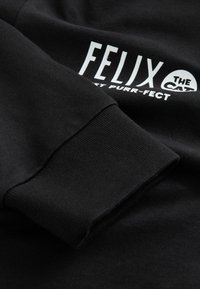 Schwarzer Sweatshirt mit gerippten Bündchen, ausgestattet mit weißem Text: "FELIX THE CAT" und "Purr-fect" in einer verspielten Schriftart. Weiche Stofftextur.