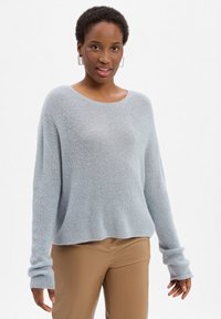 Lichtblauwe oversized trui van zacht, gestructureerd materiaal met een brede halslijn en lange mouwen, gecombineerd met beigekleurige, nauwsluitende broek.