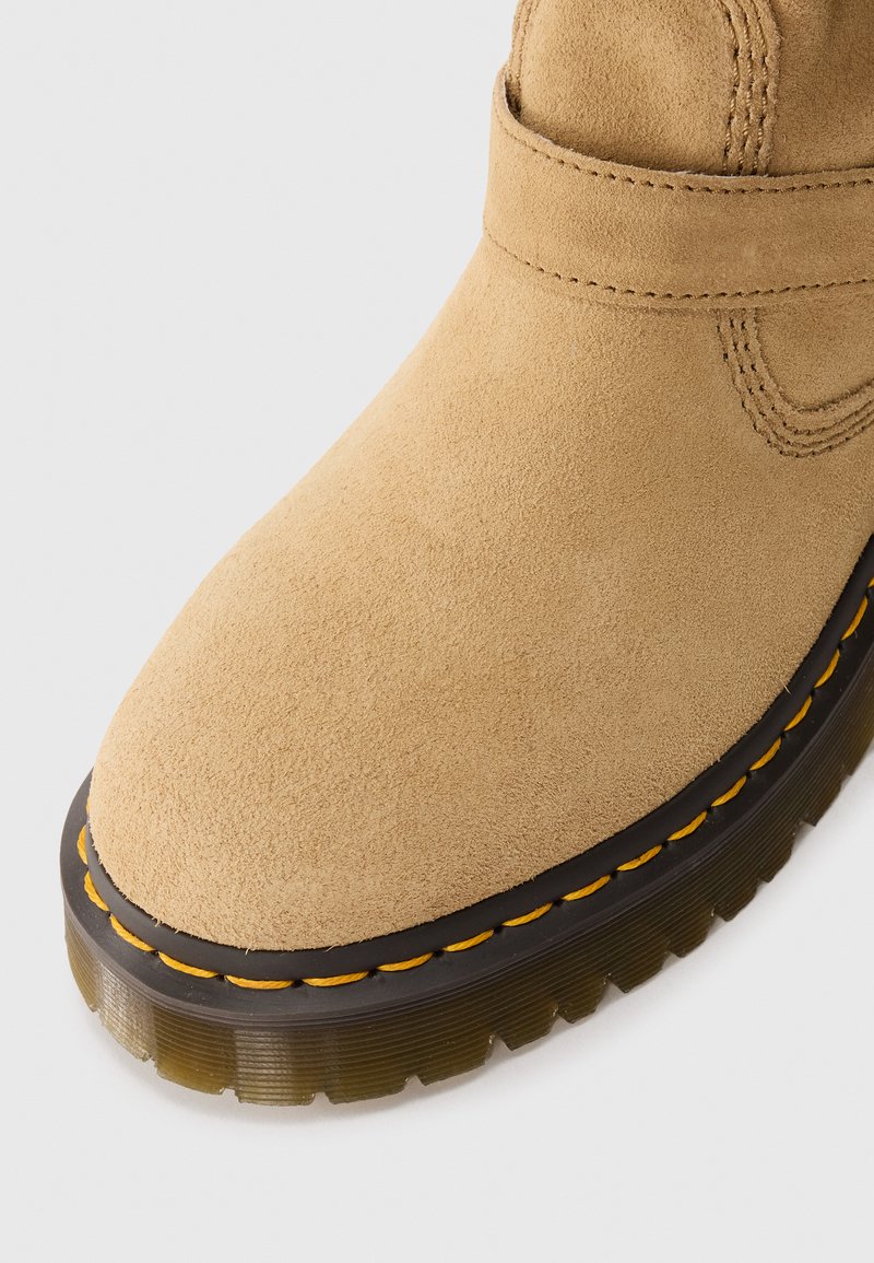Bottine en daim beige avec un bout arrondi, dotée d'une semelle en caoutchouc noir et de surpiqûres jaunes le long de la couture. Texture lisse dans l'ensemble.