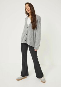 Grå stickad cardigan med lös passform, med en v-ringning och fem svarta knappar, i kombination med svarta byxor och grå sneakers.