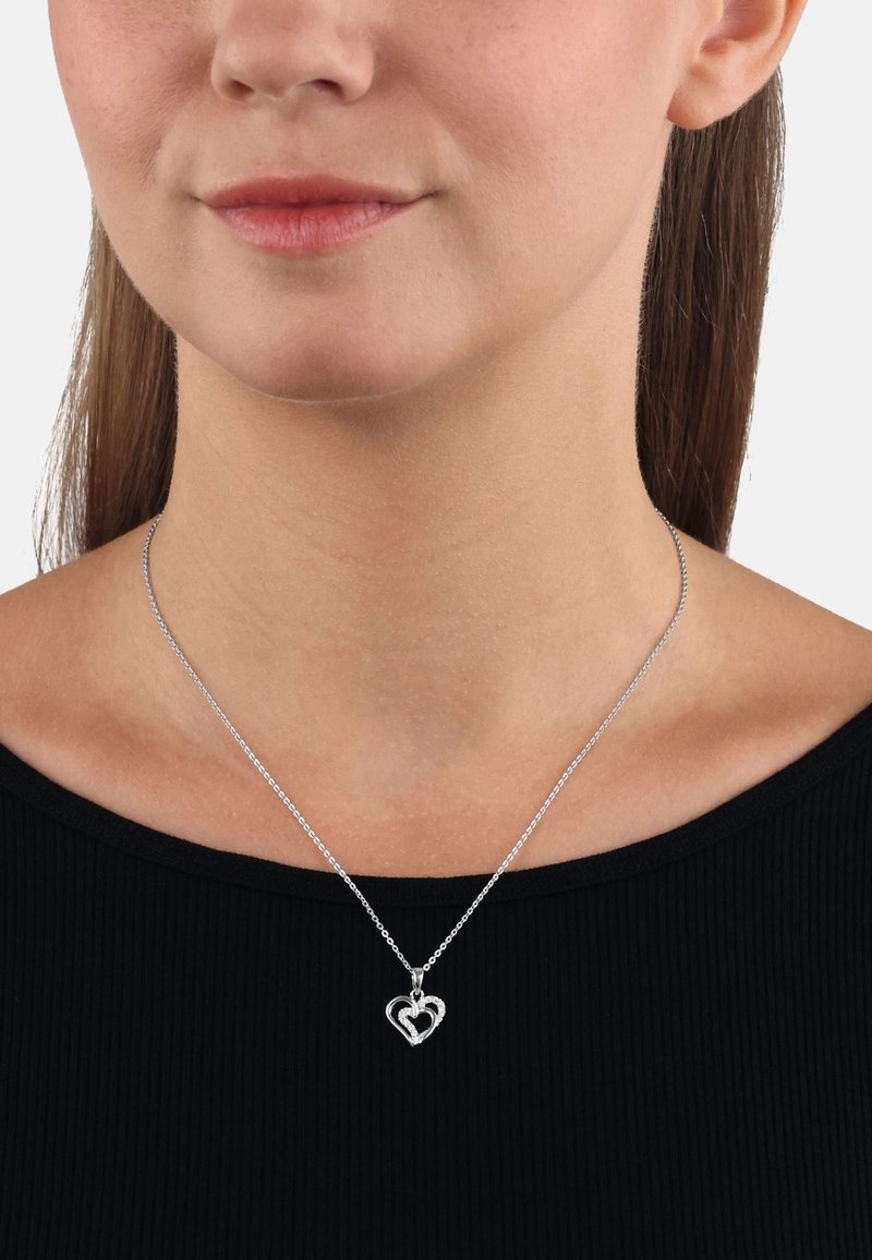 Sömlös silverhjärt-halsband med ihopflätad design, tunn kedja och polerad yta, bärs på nyckelbenet ovanför en svart topp.