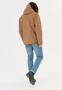 Brun huva jacka med en avslappnad passform, kombinerad med ljusblå jeans och svarta anklar stövlar, med en slät, matt yta.