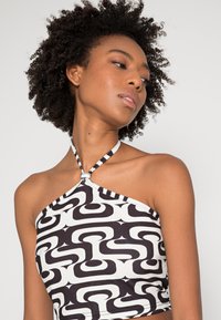 Top halter neck em preto e branco com um padrão geométrico de formas ousadas, textura de tecido suave e um detalhe listrado na gola.
