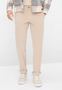Pantaloni in corduroy beige con una vestibilità dritta, dotati di chiusura a bottone, tasche laterali e orli arrotolati, abbinati a sneakers di colore chiaro.