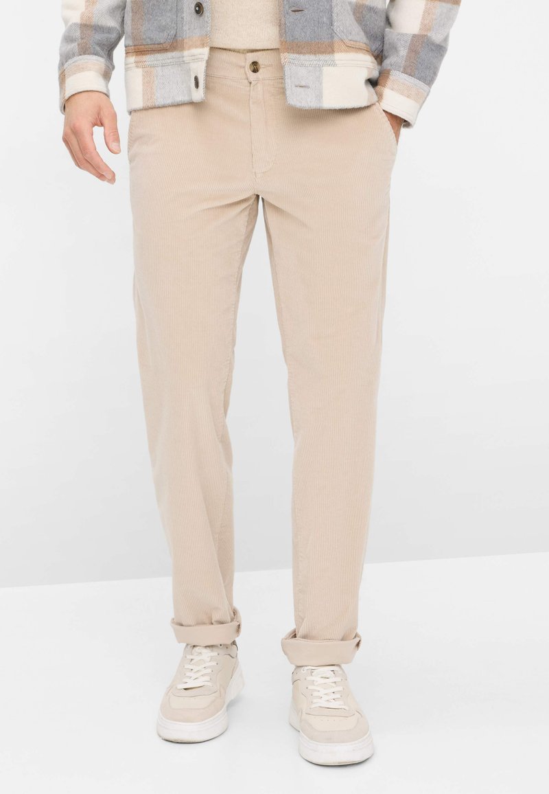 Pantaloni in corduroy beige con una vestibilità dritta, dotati di chiusura a bottone, tasche laterali e orli arrotolati, abbinati a sneakers di colore chiaro.