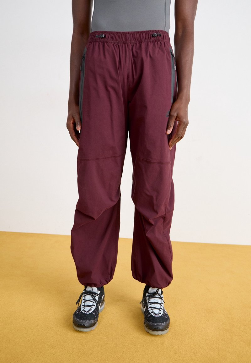 Bordeauxkleurige broeken met een elastische tailleband, zijzakken en een gestructureerde stof. Draagt u met zwarte schoenen met witte veters en accenten.