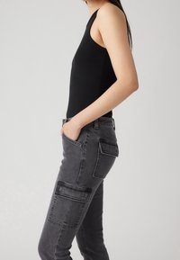 Top sin mangas de canalé negro con un diseño ajustado, combinado con pantalones cargo gris oscuro que cuentan con bolsillos laterales y una textura suave.