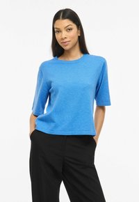 Haut bleu à manches courtes en tissu doux. Présente un col rond et une coupe décontractée, associé à un pantalon noir.