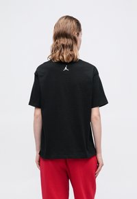 T-shirt nera a maniche corte in cotone, con il logo bianco di Jordan sulla parte posteriore near il colletto. Tessuto morbido e vestibilità comoda.