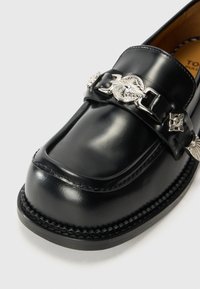 Schwarze Lederloafer mit glatter Oberfläche, rechteckiger Zehenform, robustem Absatz und dekorativen silberfarbenen Beschlägen am Riemen.