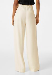 Crème brede broek met een elastische tailleband en één achterzak. De stof lijkt glad en lichtgewicht, ideaal voor casual dragen.