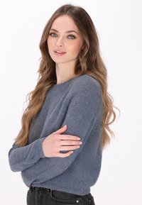 Helles blaues gestricktes Sweatshirt mit strukturiertem Muster, Rundhalsausschnitt und langen Ärmeln, über dunklen Jeans getragen. Weiche, lässige Passform.