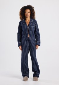 Ensemble de pyjama rayé bleu marine composé d'une veste courte avec fermeture à nouer et d'un pantalon ample assorti avec des ourlets retroussés. Matière douce.