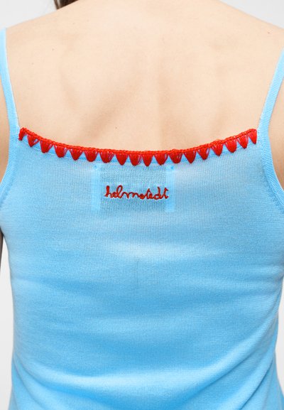 Πίσω όψη ατόμου που φοράει ανοιχτό μπλε αμάνικο τοπ με κόκκινο κεντητό κείμενο και κόκκινο περίγραμμα κατά μήκος της πάνω άκρης.