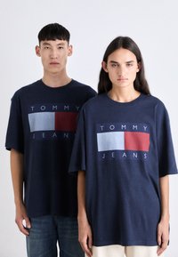 Camisetas oversized de color azul marino con un diseño gráfico central. Presenta paneles rectangulares en rojo, blanco y azul con el texto "TOMMY JEANS".