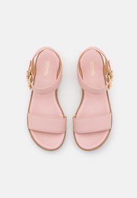 Roze leren sandalen met twee brede banden en een zijsluiting. De zool is plat met een natuurlijke textuur, wat een minimalistisch ontwerp benadrukt.