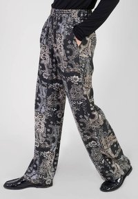 Pantalons noirs à motif paisley avec une coupe décontractée, une taille élastique et des poches latérales, mettant en valeur des motifs complexes en argent et beige.