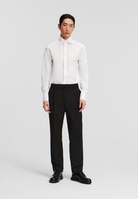 Biela košeľa s dlhým rukávom a gombíkmi skombinovaná s čiernymi nohavicami s elastickým pásom. Čierne topánky dotvárajú outfit. Minimalistický dizajn.