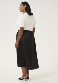 Zwarte midi-rok met een elastische tailleband, gemaakt van soepel materiaal. Gepaard met een aansluitend wit topje, dat een nette silhoeët laat zien.
