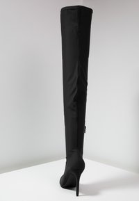Bota negra hasta la rodilla hecha de material suave, con un alto tacón de aguja, detalles de costura vertical y un diseño ajustado.