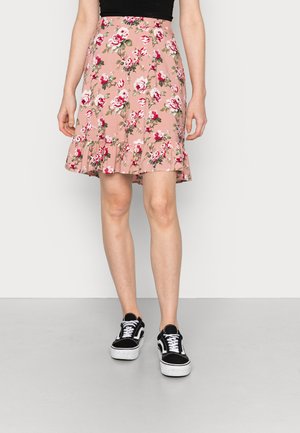 A saia floral apresenta uma base rosa com grandes flores brancas e vermelhas, uma bainha godê e uma renda em camadas na parte inferior. Combinada com ténis pretos.