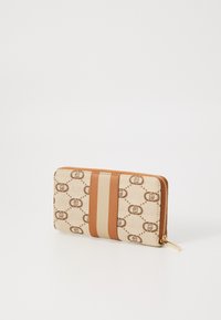 Wallet featuring a beige canvas body with brown logo pattern, a smooth tan leather stripe, and a gold zipper closure.