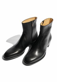 Botas de tobillo de cuero negro con una textura suave, puntera redondeada, cierre con cremallera lateral y forro interior marrón. Tacones bajos tipo bloque.