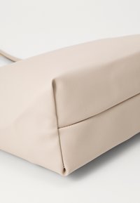 Sac à main rectangulaire beige fabriqué en tissu texturé, avec des lignes épurées et une couture le long de la base pour plus de structure.