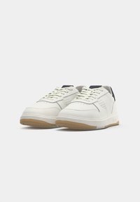 White low-top sneakers with beige soles, perforated side details, and black heel tabs, shown from front-left angle.