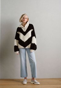 Pulover supradimensionat cu model în zigzag alb-negru, cu guler înalt, asortat cu blugi scurți de culoare albastră deschis și pantofi slip-on albi.