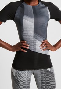 Svart och grå aktivkläder topp med en texturerad design och diagonala ränder. Kortärmad, figurnära form, tillverkad av stretchigt material.