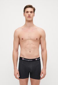 Pánske tmavošedé boxerky s čiernym pásom s bielym logom "Champion". Hladká textura, priliehavý strih, stredná dĺžka.