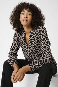 Schwarze Bluse mit einem geometrischen Muster in Beige und Rosa, mit einem Knopfverschluss-Ausschnitt und langen Ärmeln. Kombiniert mit schwarzen Hosen.