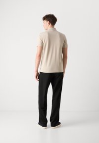 Beige polo skjorte med korte ermer, tettsittende passform og myk tekstur. Svarte bukser med avslappet passform og kremfargede sko med blå detaljer.