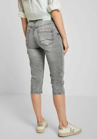 Jeans de mezclilla gris recortados con un desvanecimiento sutil, bolsillos traseros y un diseño ajustado. Combinados con zapatillas blancas con acentos en beige claro.