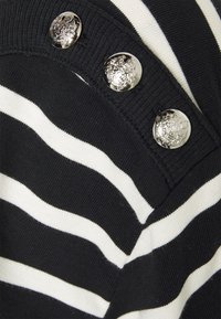 Svetr s černobílými pruhy, kulatým výstřihem a třemi kovovými knoflíky s dekorativním emblémem na ramenním švu.