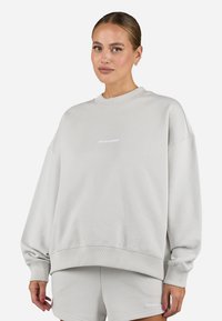 Light grey oversized sweatshirt made of soft fabric. Features a crew neck, ribbed cuffs, and a small white logo on the chest.