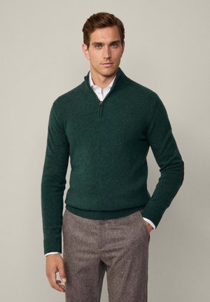 Dark green zip-neck sweater made of soft knit material, featuring ribbed cuffs and hem, worn over a white collared shirt.
