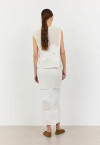 Vitt stickat tvådelat set bestående av en ärmlös topp med blommönster och en matchande lång kjol. Mjuk textur och luftig design.