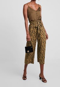 Top in satin verde oliva con bottoni, abbinato a culotte marroni a fantasia e una borsa strutturata nera. Sandali neri con streep completano il look.