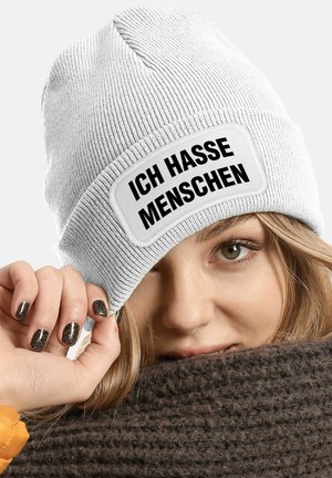 White knit beanie with a folded cuff featuring a rectangular patch that reads "ICH HASSE MENSCHEN" in bold black letters.