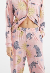 Conjunto de pijama rosa con un diseño de leopardo y motivos de sol y luna. Tejido suave, camisa de botones con bolsillo, pantalones con cinturilla elástica.