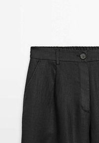 Svarta linnebyxor med en åtsittande midja, framknappstängning och sidfickor. Materialet har en slät textur och en ren, skräddarsydd design.