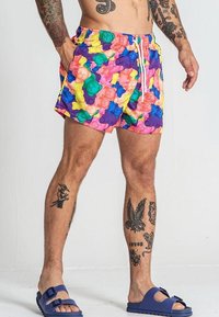 Shorts de bain colorés arborant un motif de oursons en gélatine dans des teintes de rose, violet, vert et jaune. Taille à cordon de serrage et tissu léger.