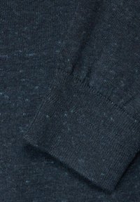 Stickad mörkblå tröja med en texturerad yta, med ljusare blå fläckar. Ärmarna är ribbade och åtsittande för en snug passform.