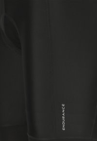 Lähikuva mustista urheilutrikooista, joissa näkyvät saumanompeleet ja pieni "ENDURANCE"-logo valkoisella tekstillä.