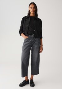 Giacca in suede nera con bottoni, top a costine nero, jeans wide-leg grigi in denim a vita alta e scarpe nere con lacci.